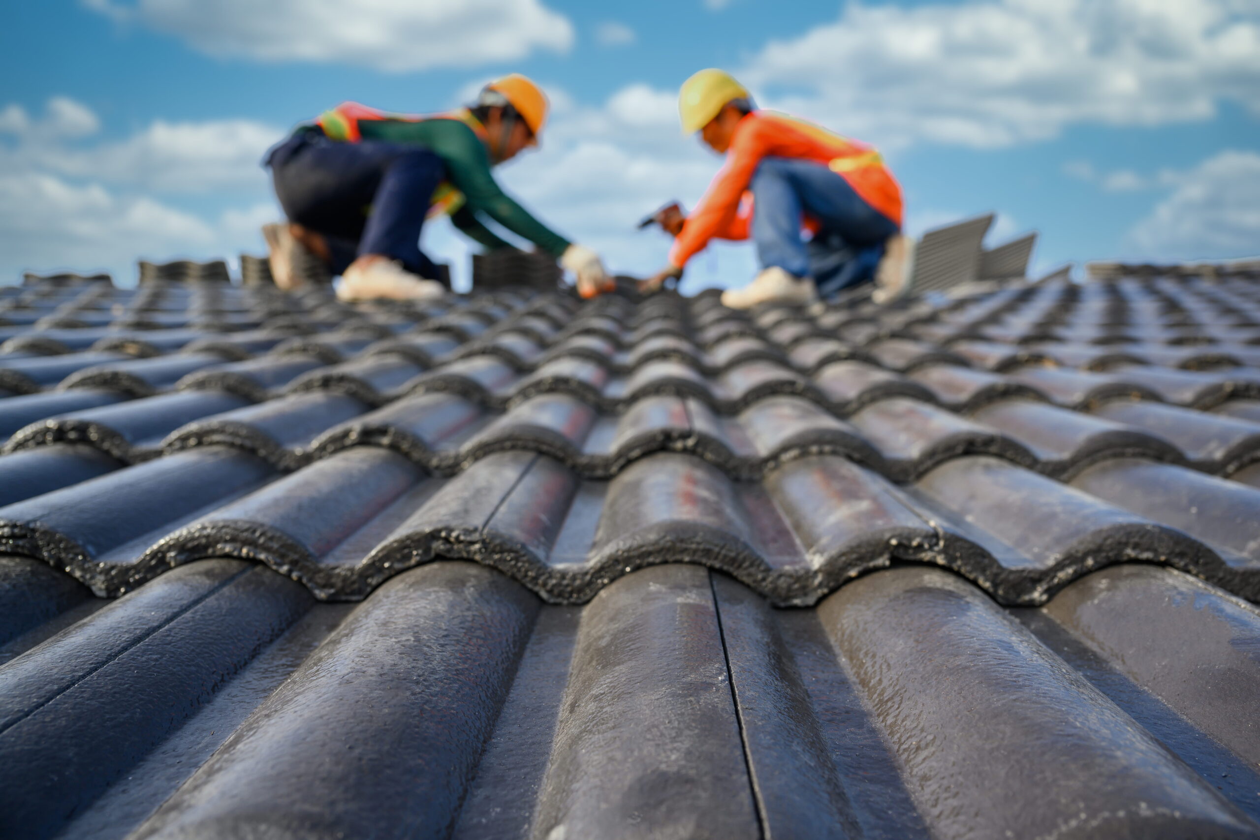 A roofer's blurry background while they work on a home's roof Drill the screws needed to secure the cement tiles using a drill. Select the focus on roof tiles.